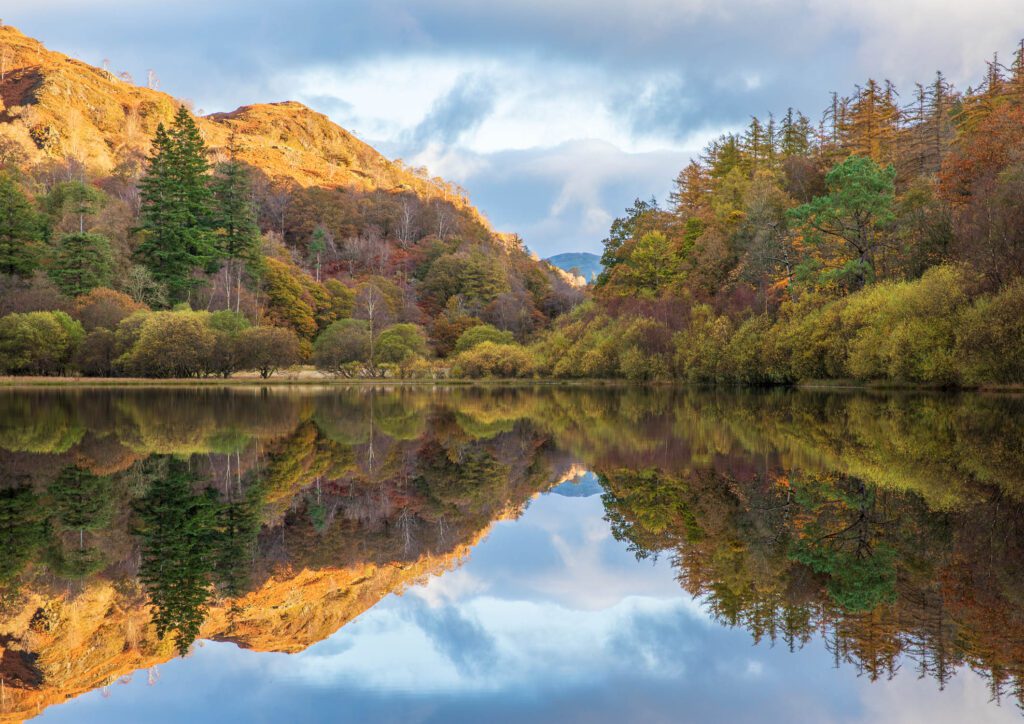 Lake District landscape photography. The Lake District is well known by landscape photographers for its spectacular autumnal colours. In this photograph, I captured just that. A beautiful morning at Yew Tree Tarn resulted in perfectly calm conditions allowing me to photograph perfectly still reflections across the tarn. The beautiful autumn colours and surrounding fells basking in the early morning light are reflected perfectly in the Tarn's water. This photograph was captured with a Canon 24-70mm F2.8L lens.