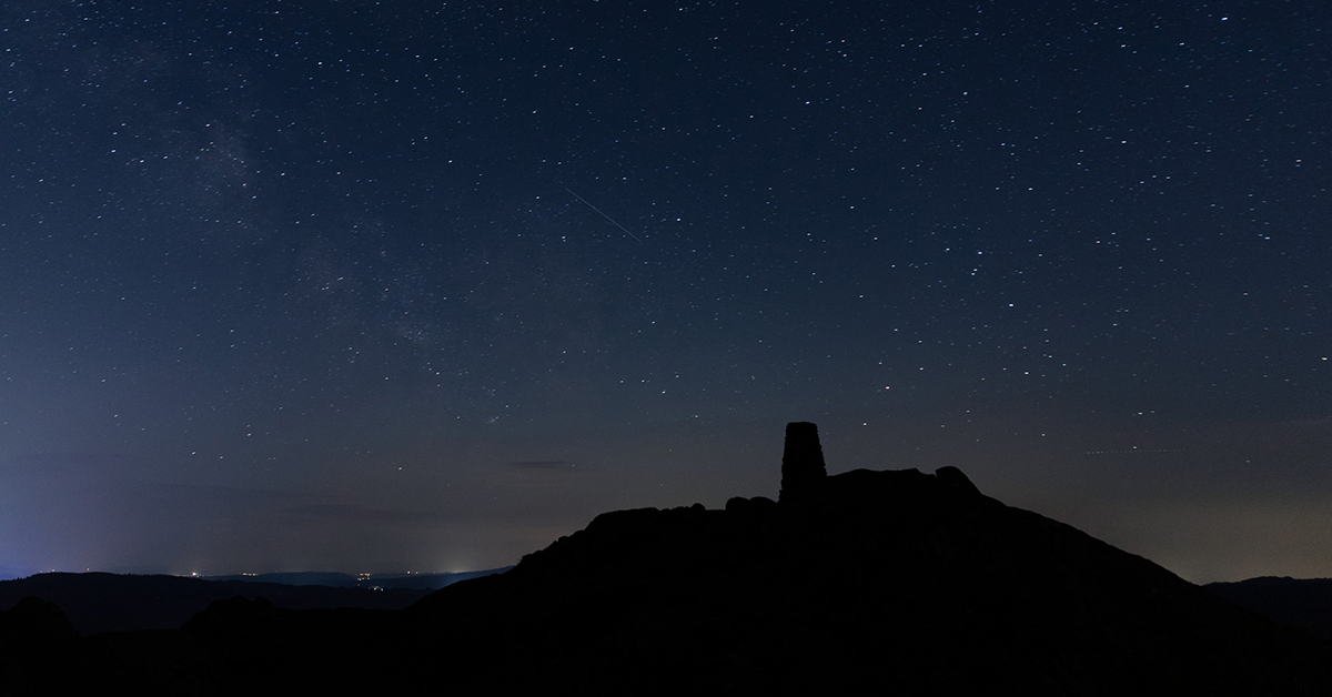 A nightscape of a starry sky and a shooting star from Black Fell in the Lake District.