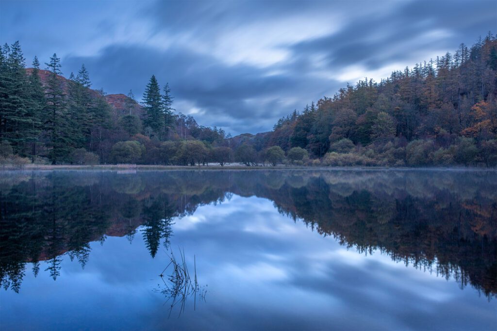 Autumn Landscape photography from the English Lake District. A stunning blue hour morning spent at Yew Tree Tarn. There was little to no wind which meant that the tarn was perfectly calm, reflecting the beautiful autumnal trees. Photographed with a Canon 5D MK4 and Canon 24-70mm F2.8L lens.