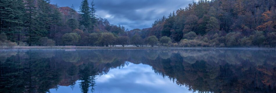 Landscape photograph of autumnal reflections during blue hour at Yew Tree Tarn in the Lake District.