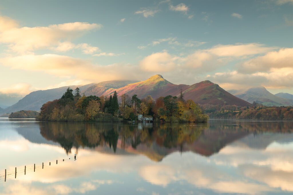 A beautiful Lake District sunrise hits the summit of Catbells whilst illuminating the surrounding clouds. Catbells stands dominantly behind a calm Derwentwater sporting stunning autumnal colours. Photographed with a Canon 5D MK4 and 24-70mm F2.8L lens.