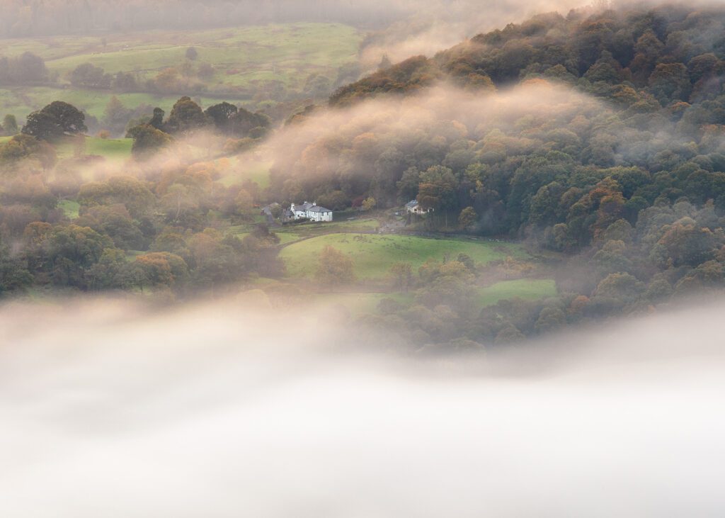 A landscape photograph from the English Lake District captured during a beautiful morning of mist. A distant farmhouse stands in solitude as surrounding mist swallows up the nearby landscape. Photographed with a Canon 5D MK4 and 24-70mm F2.8L lens.