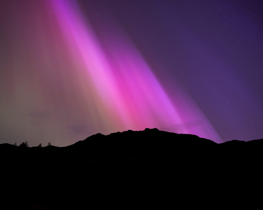 The breathtaking Northern Lights illuminate the silhouetted mountains surrounding Blea Tarn in the Lake District during a G5 geomagnetic storm.