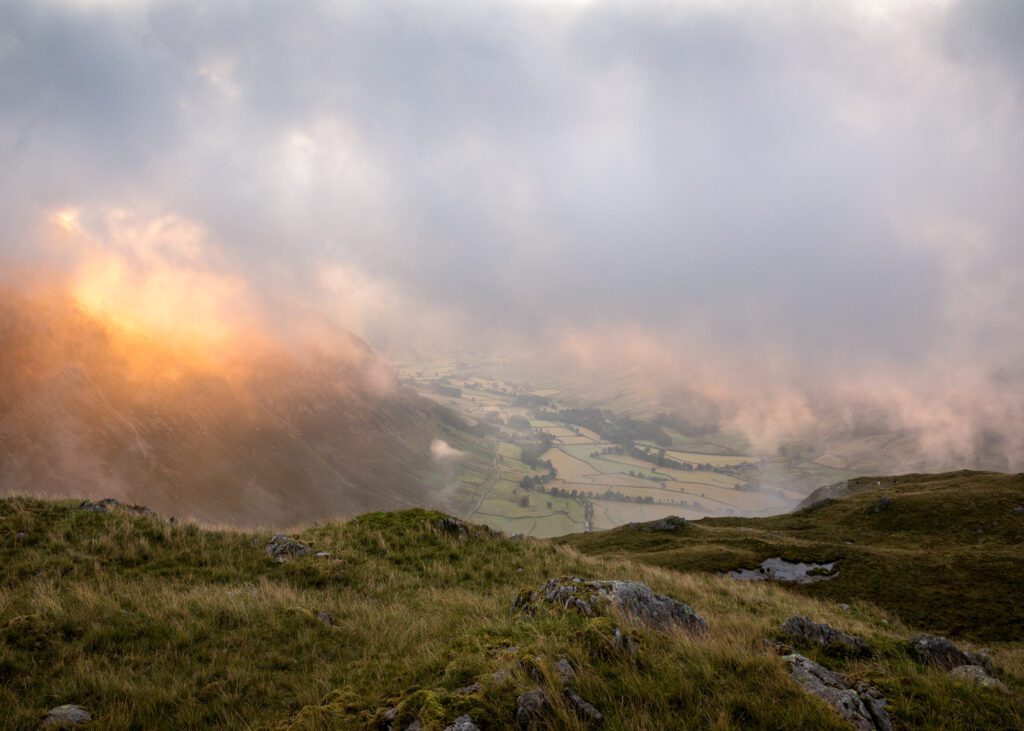 Landscape Photograph of Mickleden Valley from Bowfell during sunrise in the Lake District. Fast-moving low-level clouds catch the golden hues of the sun during the early hours of the morning.