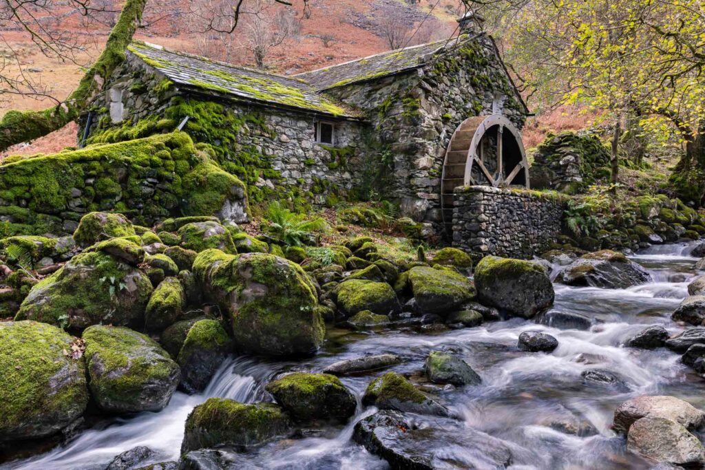 An old water mill surrounded by moss and autumnal trees, hidden away in Borrowdale Valley alongside a raging stream after heavy rainfall.