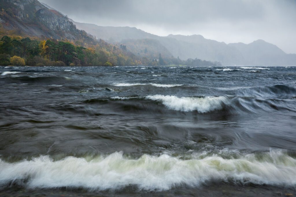 Stormy waves on Derwentwater with autumnal trees and heavy rain looming in the distance.