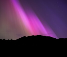 The breathtaking Northern Lights illuminate the silhouetted mountains surrounding Blea Tarn in the Lake District during a G5 geomagnetic storm.