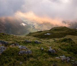 A view from the band on the ascent of Bowfell in the Lake District during a breathtaking summer morning. Low cloud hovers above Mickleden Valley catching the glorious sunrise light around Great Langdale.