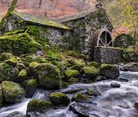 An old water mill surrounded by moss and autumnal trees, hidden away in Borrowdale Valley alongside a raging stream after heavy rainfall.