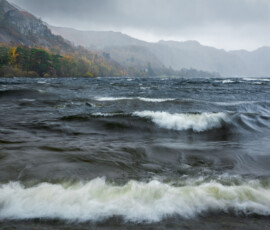 Stormy waves on Derwentwater with autumnal trees and heavy rain looming in the distance.
